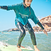 Chica surfera deslizándose sobre una pequeña ola verde